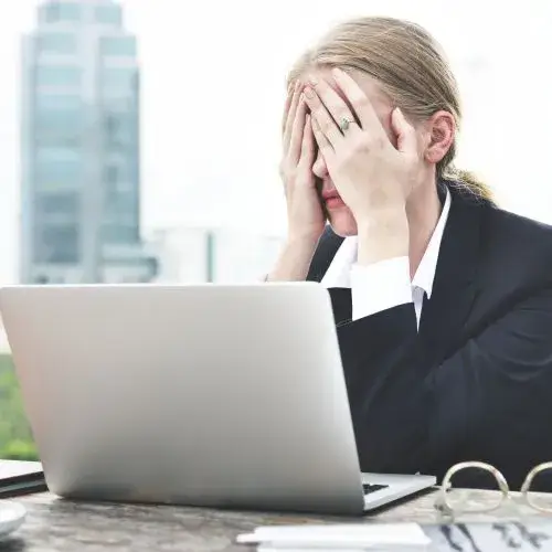 business woman sitting at laptop with her hands covering her face from stress